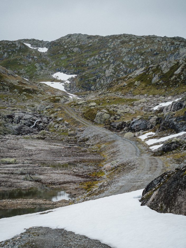As long as the road continues.. Gravel road in mountains, a few piles of snow
